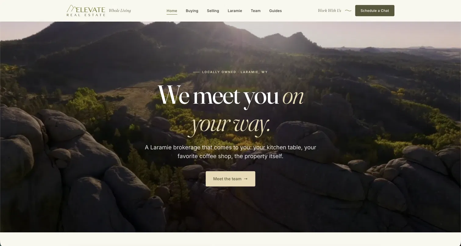 The Elevate Real Estate homepage: navigation over a full-width photograph of the rocks and pines above Laramie, carrying the headline We meet you on your way.
